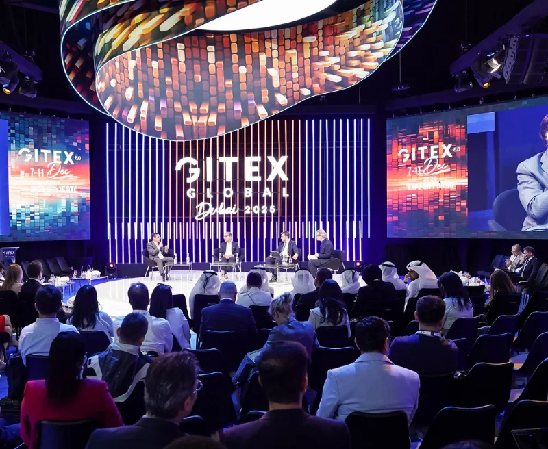 GITEX Global main stage with a panel of four speakers, a curved LED sculpture overhead and a seated audience
